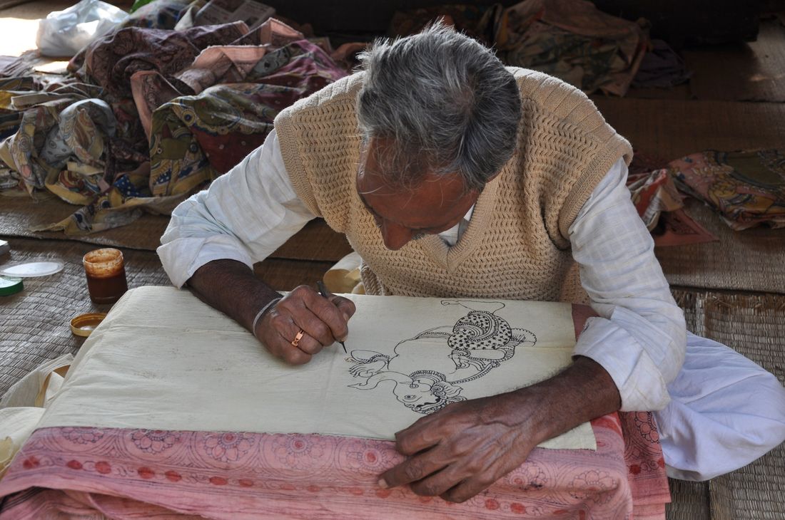 A Kalamkari artist drawing on cloth with a bamboo pen