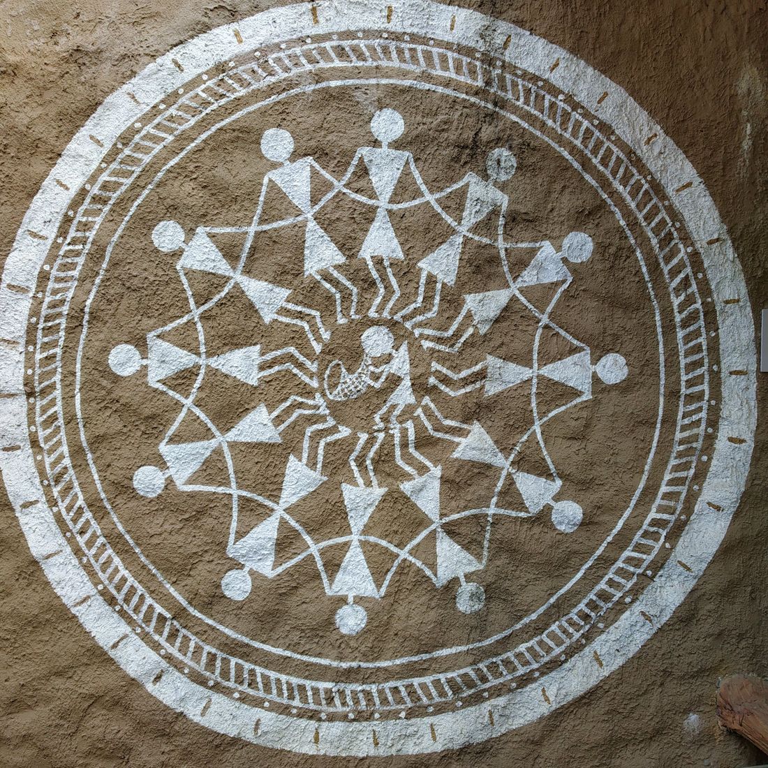 A Warli painting of the tarpa dance circle in white on a mud wall